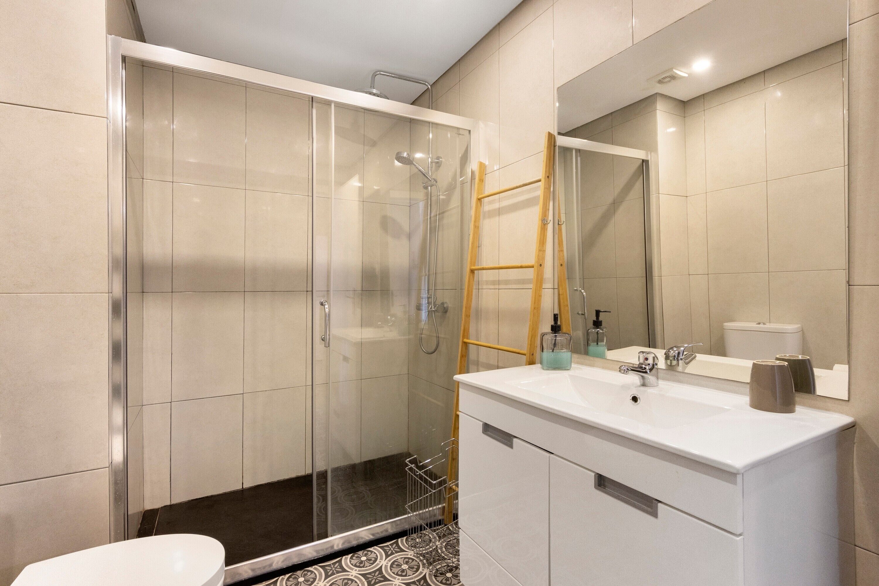 A modern bathroom with a glass shower enclosure, a white vanity, and a mirror above the sink.