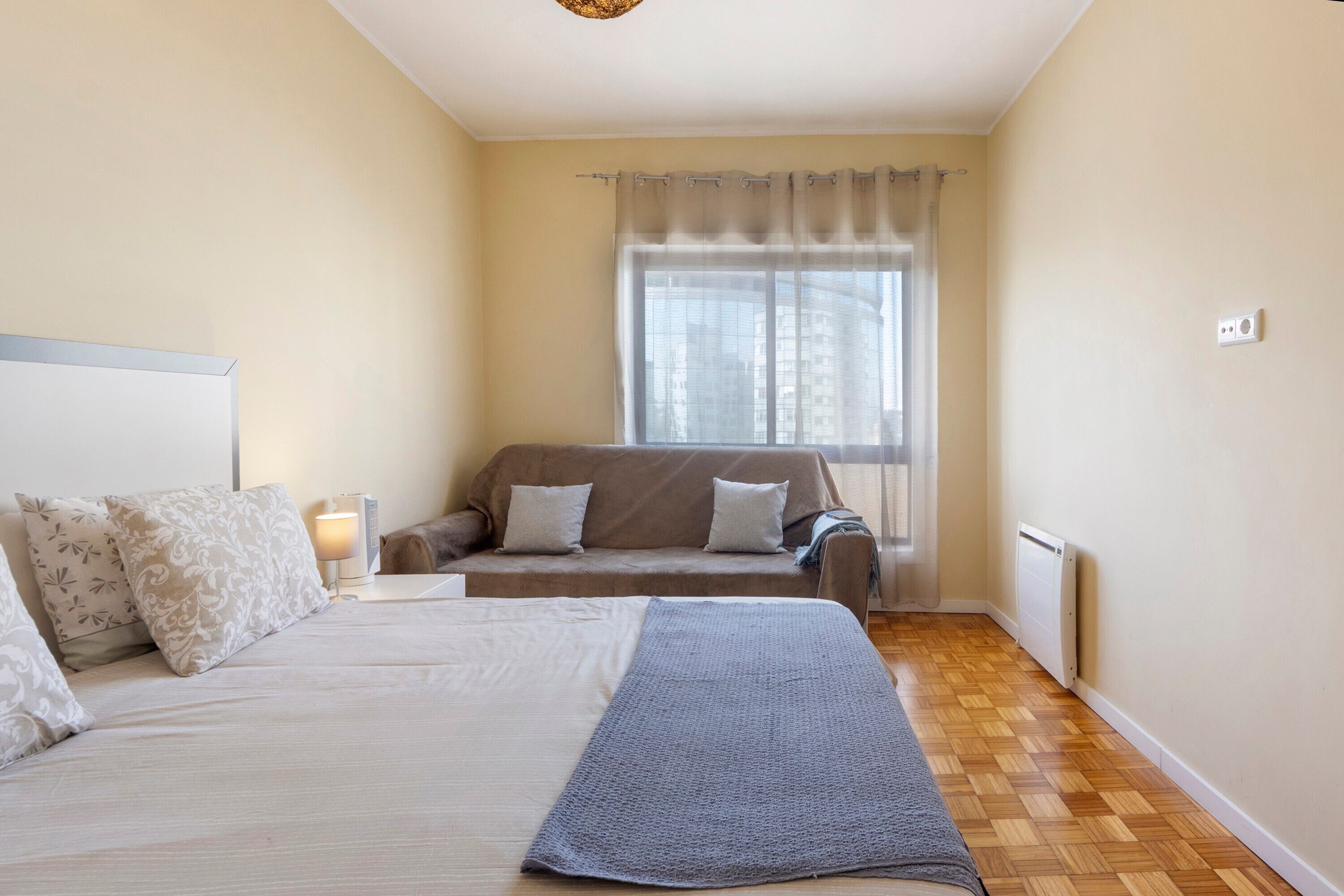 Ein Schlafzimmer mit einem Bett, einer Couch, einem Fenster mit Vorhängen und einer Heizung.