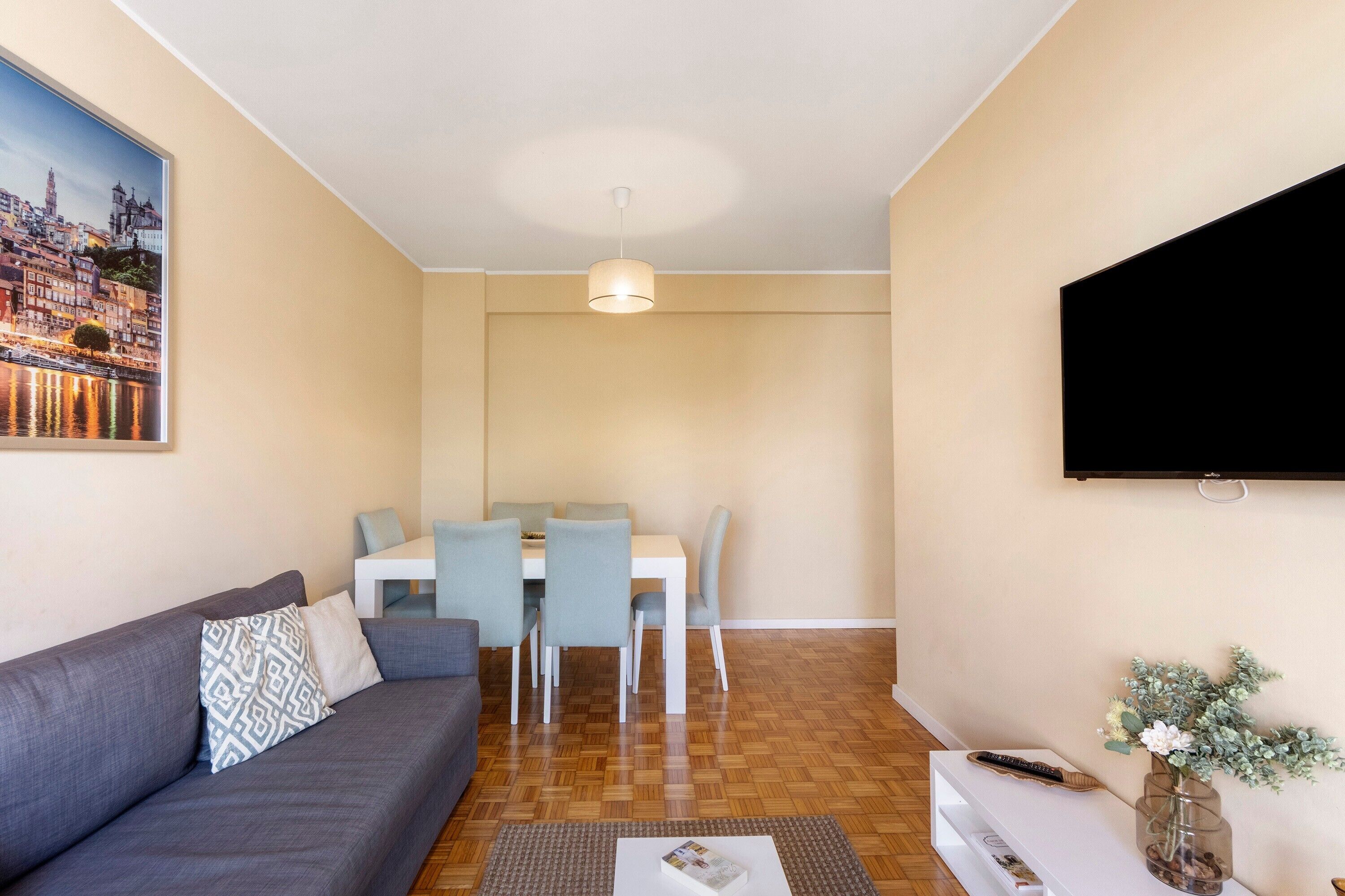 Un espacio habitable compacto con un sofá, una mesa de comedor, sillas, un televisor de pantalla plana y un pequeño jarrón decorativo.