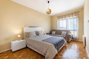 Une chambre à coucher comprenant un lit, une table de chevet, une lampe, un canapé et une fenêtre avec des rideaux.