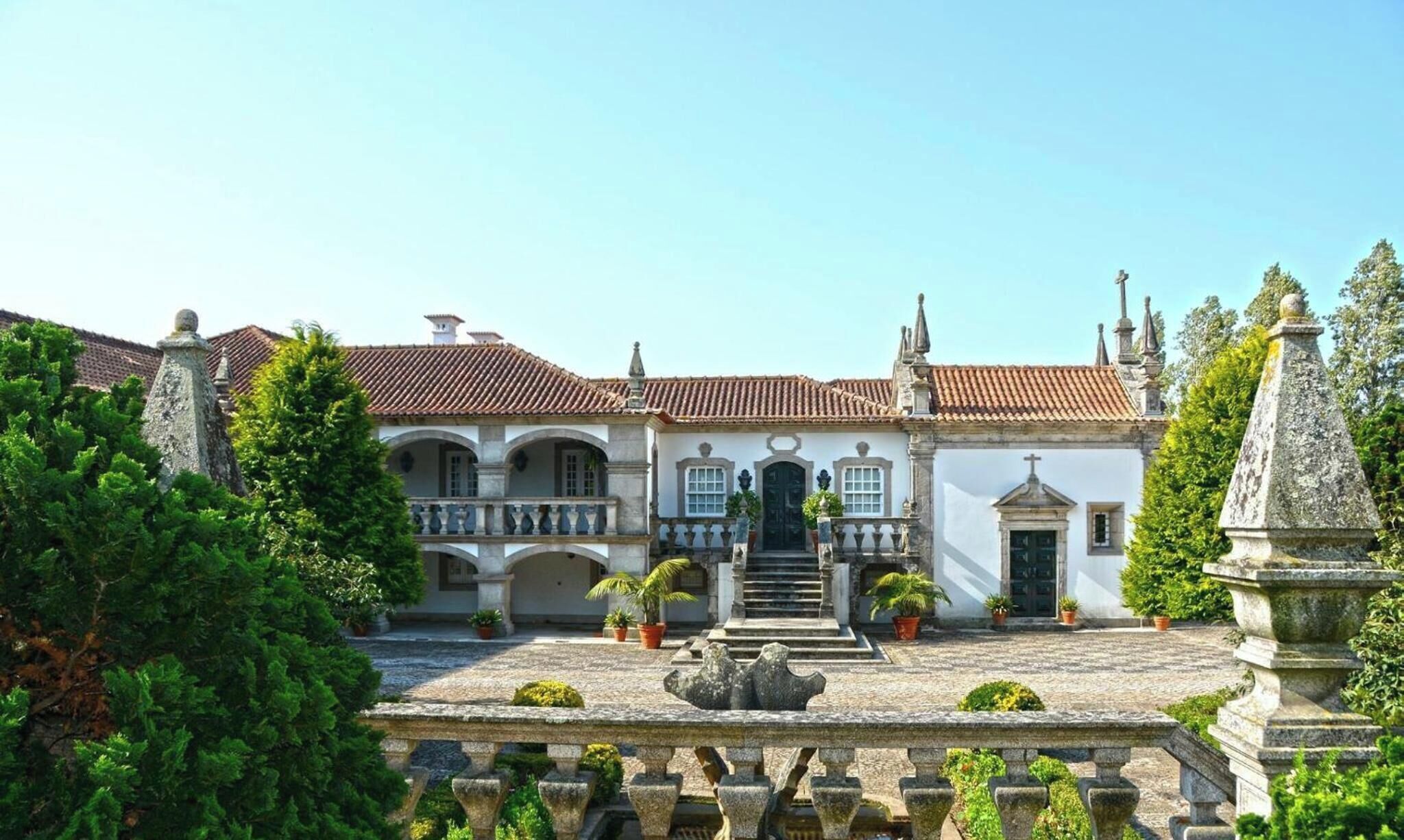 Um edifício histórico com uma escadaria central, janelas em arco e telhado telhado.
