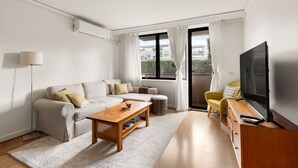 Una sala de estar moderna con sofá, mesa de centro, televisor y un balcón con cortinas.