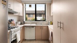 Cocina compacta con estufa a gas, lavavajillas y ventana con vistas a un barrio residencial.