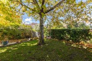 Une cour bordée d’arbres, avec une balançoire, un chemin pavé et une haie.
