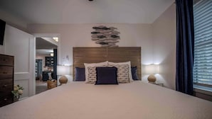 A bedroom with a large bed, a wooden headboard, two bedside lamps, and a wall art piece above the bed.