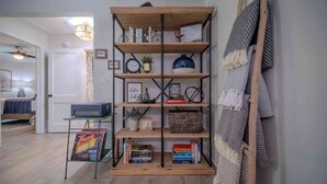 A room with a wooden bookshelf, a small table with a lamp, and a wall-mounted rack with a patterned cloth.