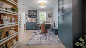 A modern kitchen with a dining area, wooden shelves with books, and a large cabinet.