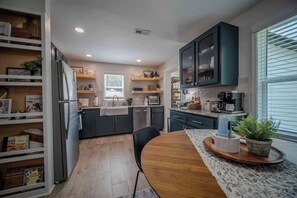 A modern kitchen with dark cabinetry, a central island, and a dining area with a wooden table.