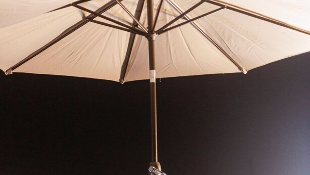 An outdoor seating area with a table and chairs under a large umbrella, overlooking a cityscape at night.