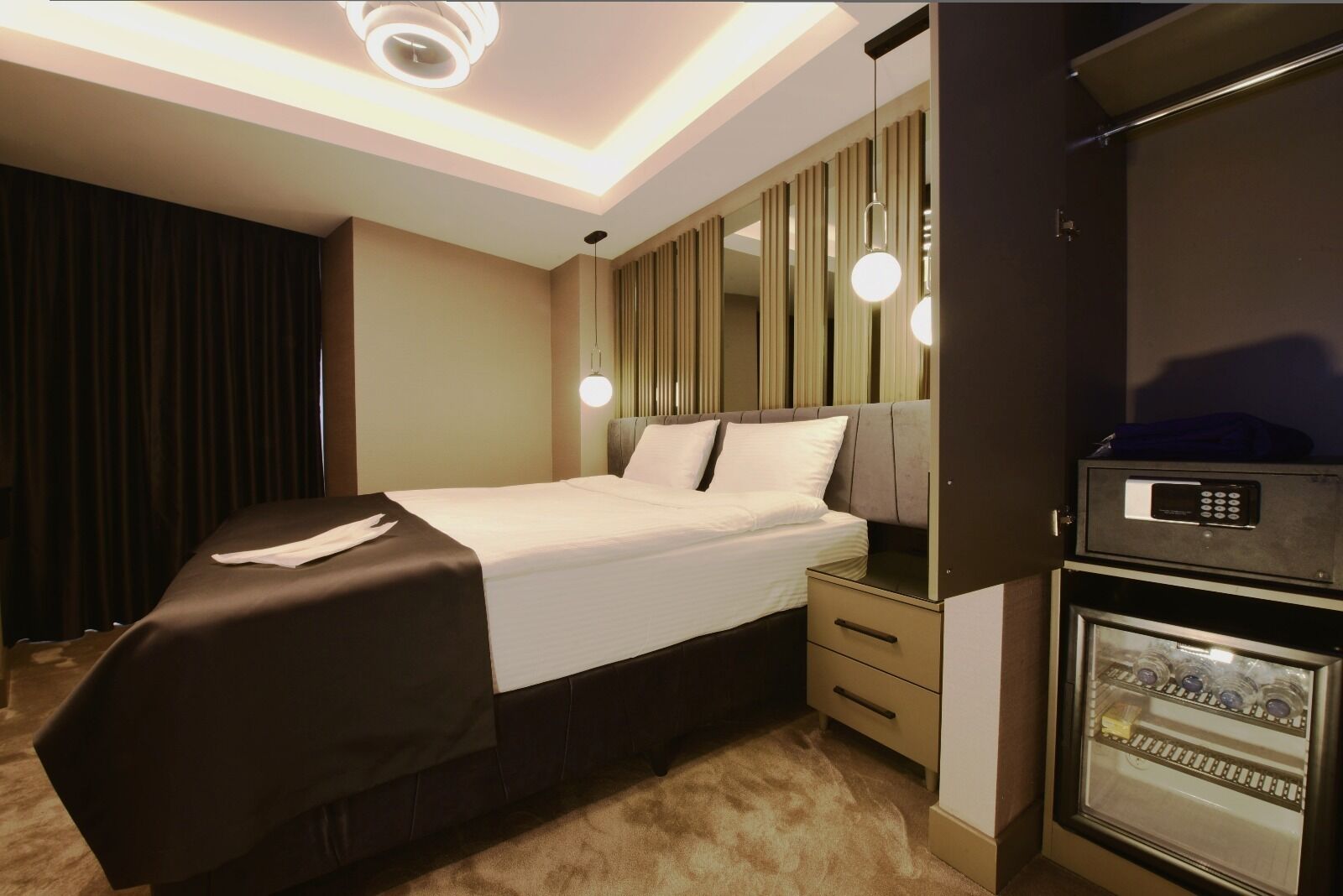 Ein Hotelzimmer mit Bett, Nachttischen, einer Minibar und einem Spiegel.