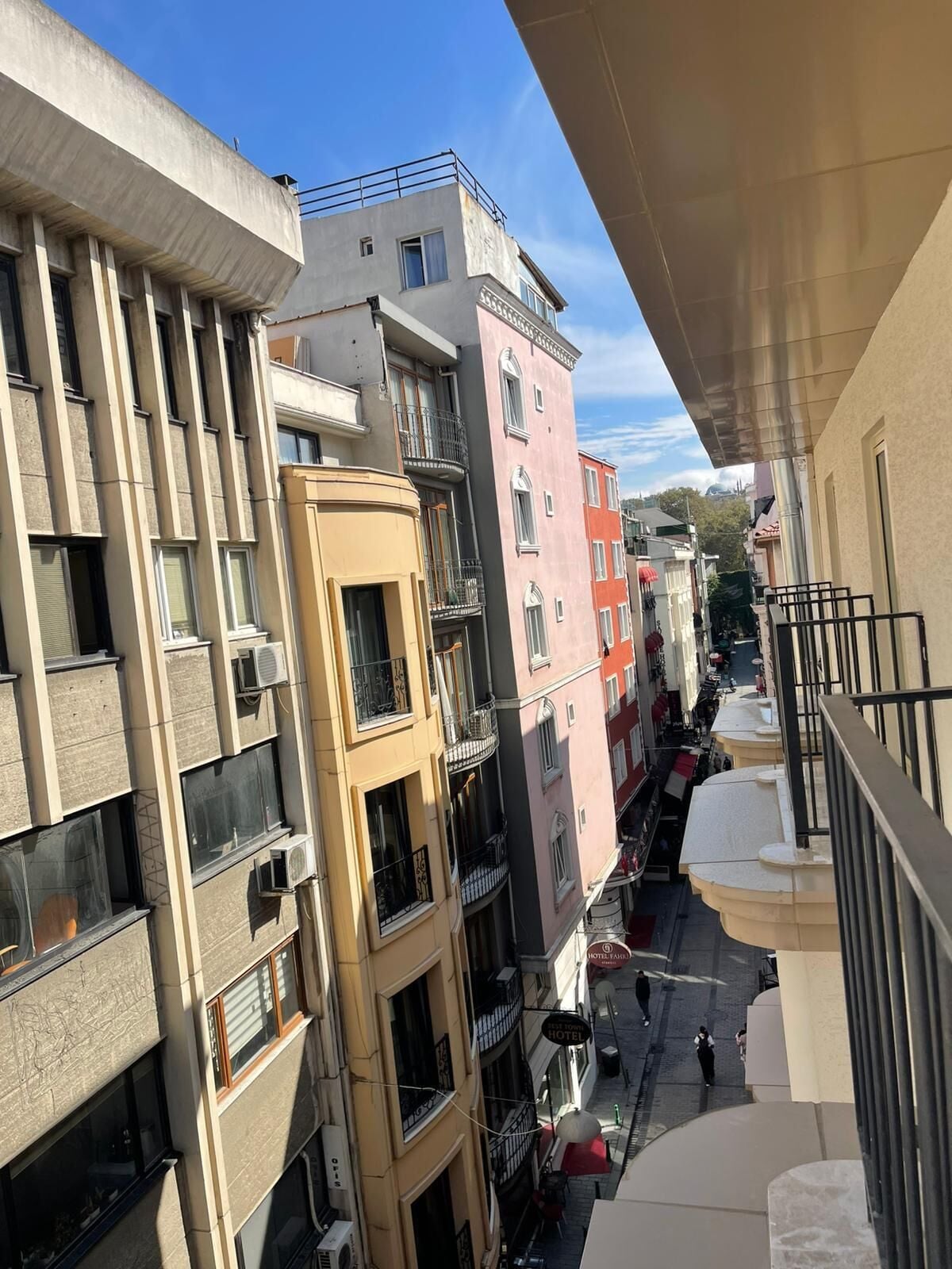 Um edifício com várias andares, varandas, uma rua abaixo e céu claro.