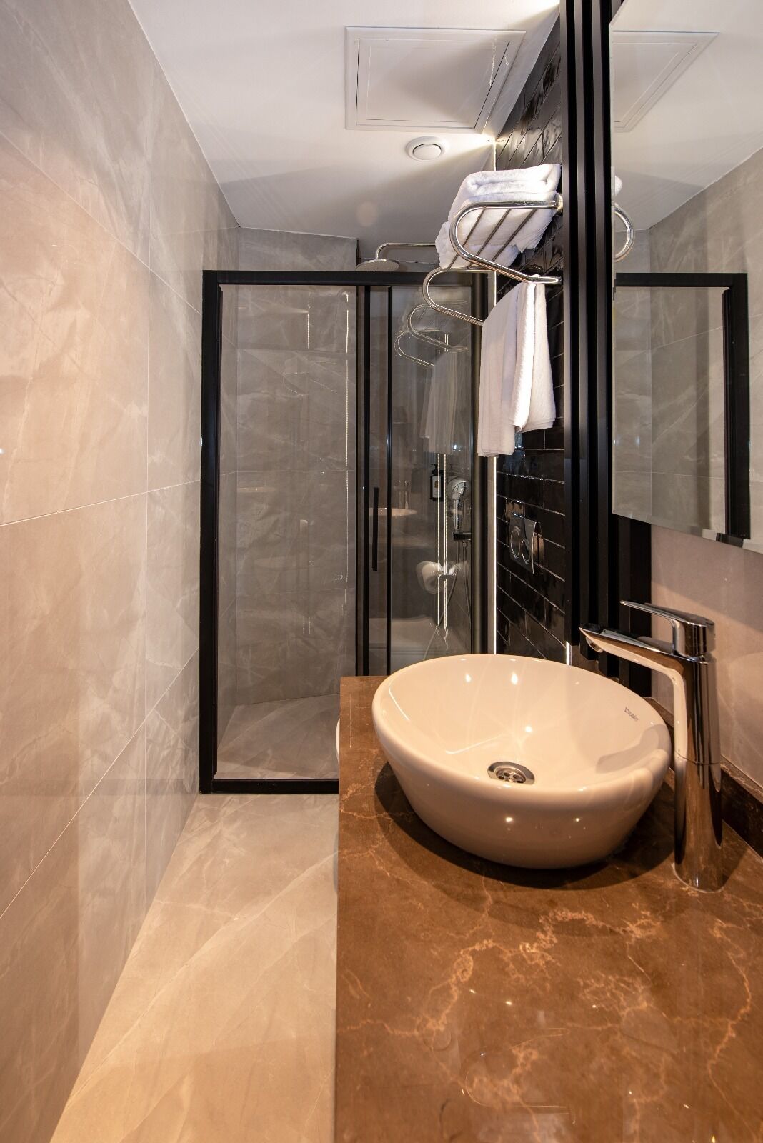 Un baño moderno con ducha de vidrio, un lavamanos ovalado grande y un espejo con marco negro.