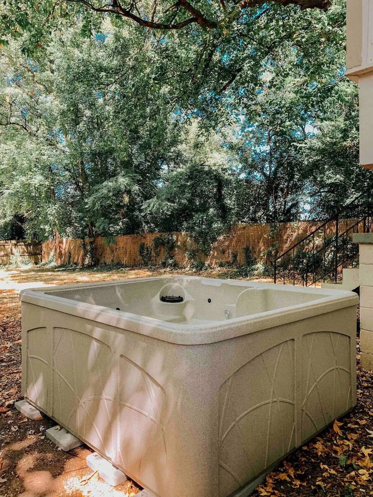 A hot tub in a garden with trees and a wooden fence in the background.