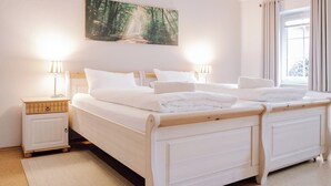 A double bed with white bedding, two bedside tables with lamps, a painting of a forest on the wall, and a window with curtains. - Cozy vacation homes and apartments - here you will find peace and relaxation (Emstek)