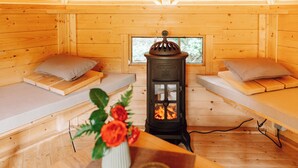 A cozy cabin interior with two wooden beds, a central wood-burning stove, and a window with a view of greenery. - Cozy vacation homes and apartments - here you will find peace and relaxation (Emstek)