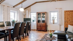 A spacious living room with a dining area, wooden beams, a cabinet, and a fireplace. - Cozy vacation homes and apartments - here you will find peace and relaxation (Emstek)