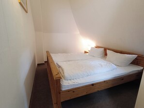 A single wooden bed with white bedding in a room with white walls and a sloped ceiling.
