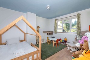 A child's room with a wooden bed, a giraffe toy, a small table, chairs, and a window with curtains.
