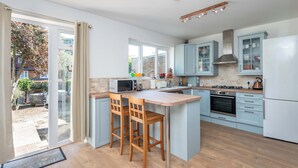 A modern kitchen with a central island, wooden chairs, a microwave, and a stove. - Spacious 3BDR Home with Workspace in Prime Spot (Greater London)