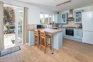 A modern kitchen with a central island, wooden chairs, a microwave, and a stove.