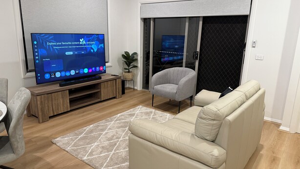 Una sala de estar moderna con un televisor de pantalla plana sobre un mueble de madera, un sillón gris, un sofá beige y una alfombra estampada.