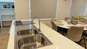 Una cocina moderna con un lavamanos de acero inoxidable, una estufa empotrada y un comedor con una mesa redonda y sillas.
