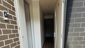 Un pasillo con piso de madera, un felpudo y una puerta con mosquitero.