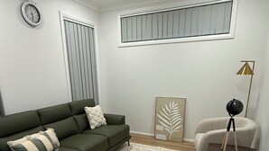 Una sala moderna con un sofá verde, un sillón beige, un tapete estampado, una lámpara de pie y un ventilador de techo.