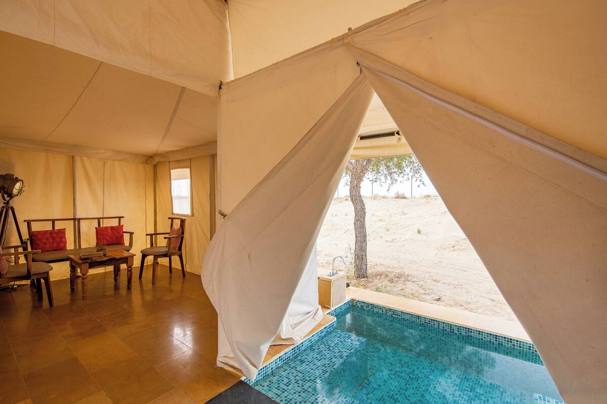 Una habitación con tienda de campaña, piscina, muebles de madera y vistas al desierto.