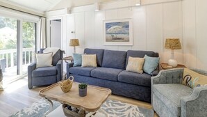 Un salón amplio con un sofá gris grande, dos sillones, una mesa de centro de madera y vistas al exterior a través de una puerta corrediza de vidrio.