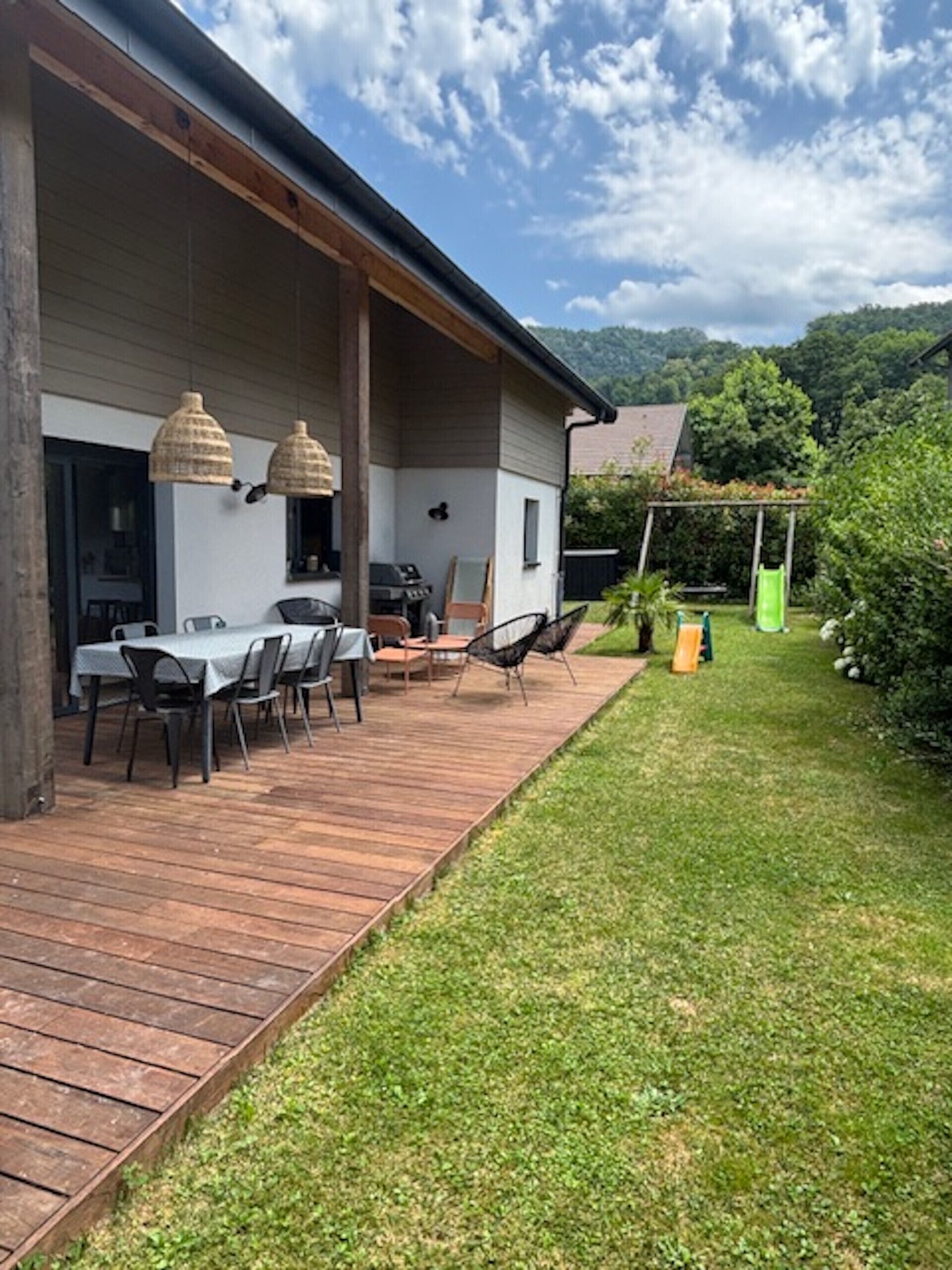 A covered patio with a table and chairs, a grill, and a pergola with a slide.