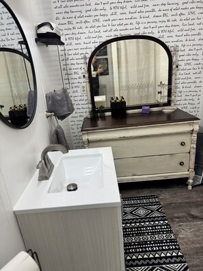 Ein Badezimmer mit einem weißen Waschbecken, zwei Spiegeln, einem Waschtisch mit Spiegel und einem gemusterten Teppich.