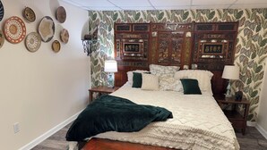Une chambre à coucher avec un grand lit, une tête de lit en bois, un banc vert et un mur décoré d’assiettes.