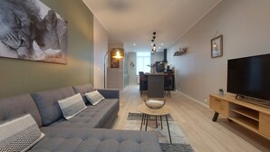 A modern living room with a grey sectional sofa, a flat-screen TV, and a dining area with a wooden table and chairs. - B As in... Forest walk (Saint-Amand-les-Eaux)