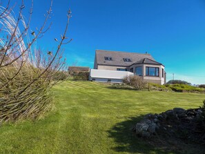 A modern house with a sloped roof, a well-maintained lawn, and a stone wall.