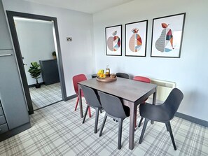 Un comedor con una mesa de madera, seis sillas y un frutero. Hay tres obras de arte enmarcadas en la pared.