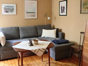 Un salon avec un canapé gris, une petite table sur laquelle se trouvent un bol et des bougeoirs, une lampe, et des œuvres d’art encadrées accrochées au mur.