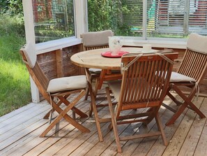 Un'area esterna con decking in legno, un tavolo rotondo e quattro sedie, delimitata da una ringhiera bianca.