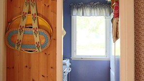 Una habitación con paredes de madera, una ventana con adornos a cuadros y un bolso colgante con motivos florales.