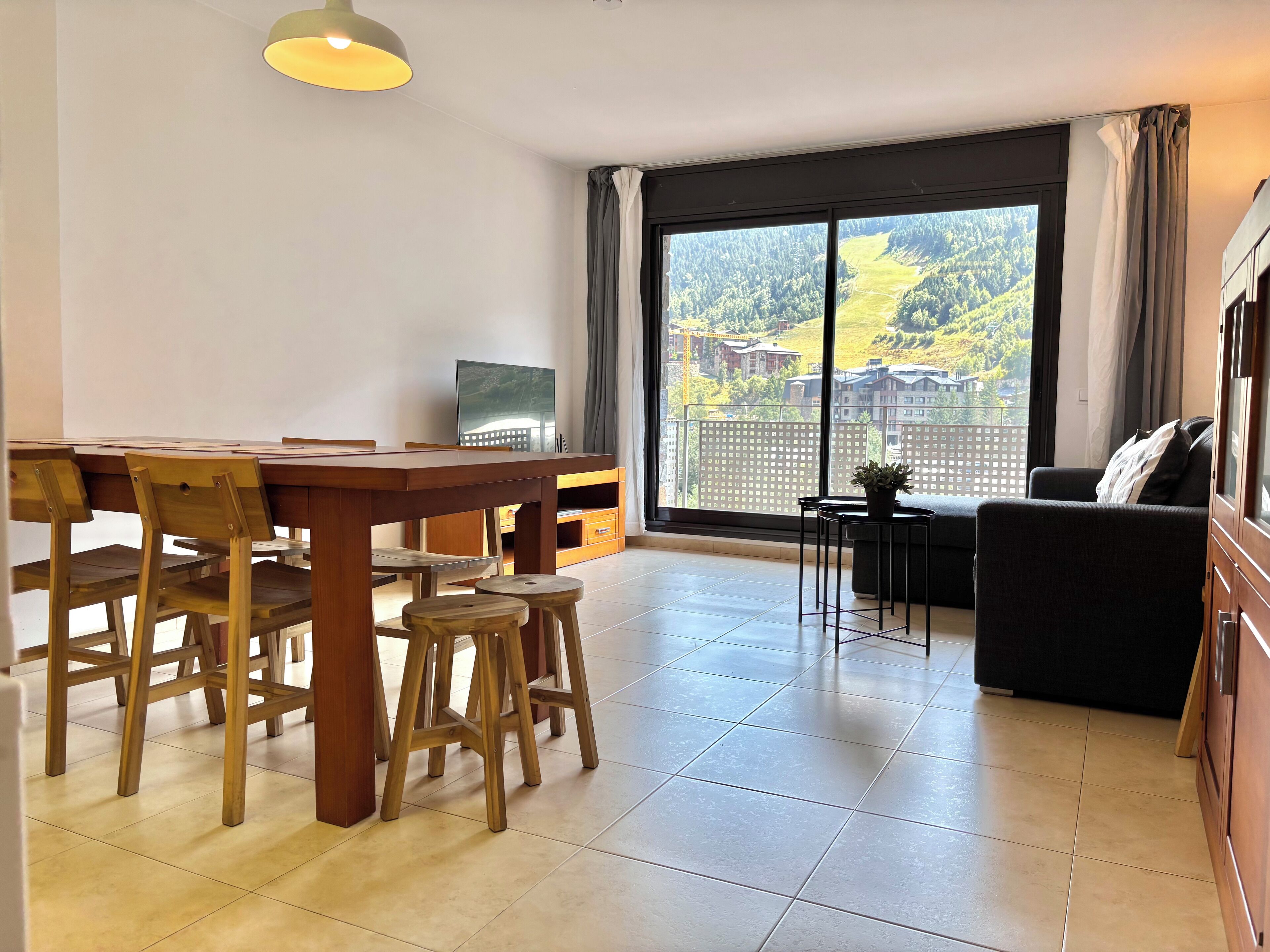 A modern living room with a dining area, large windows, and a view of a residential area.