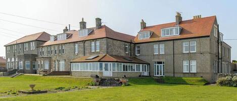 A large, multi-story stone building with a symmetrical facade, multiple chimneys, and a central glass conservatory.