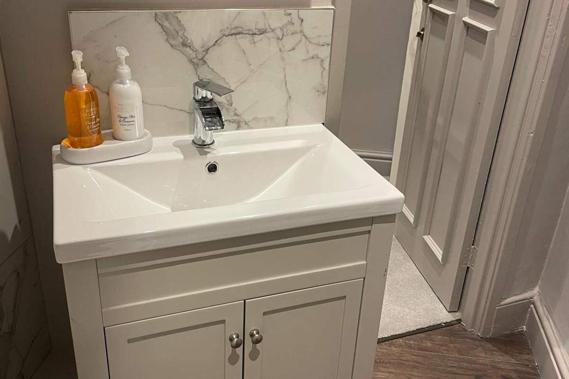A bathroom with a white sink, two bottles of liquid soap, and a marble backsplash.