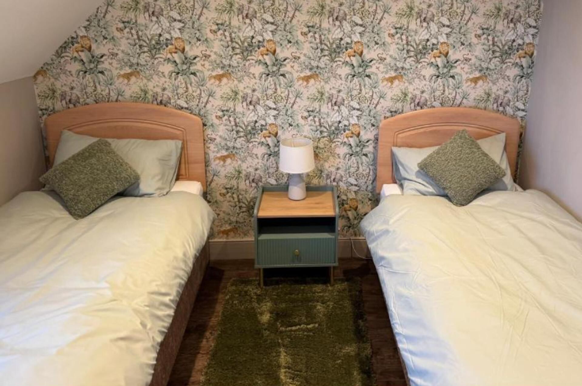 Een tweepersoonskamer met twee bedden, een nachtkastje met een lamp en bloemenbehang.
