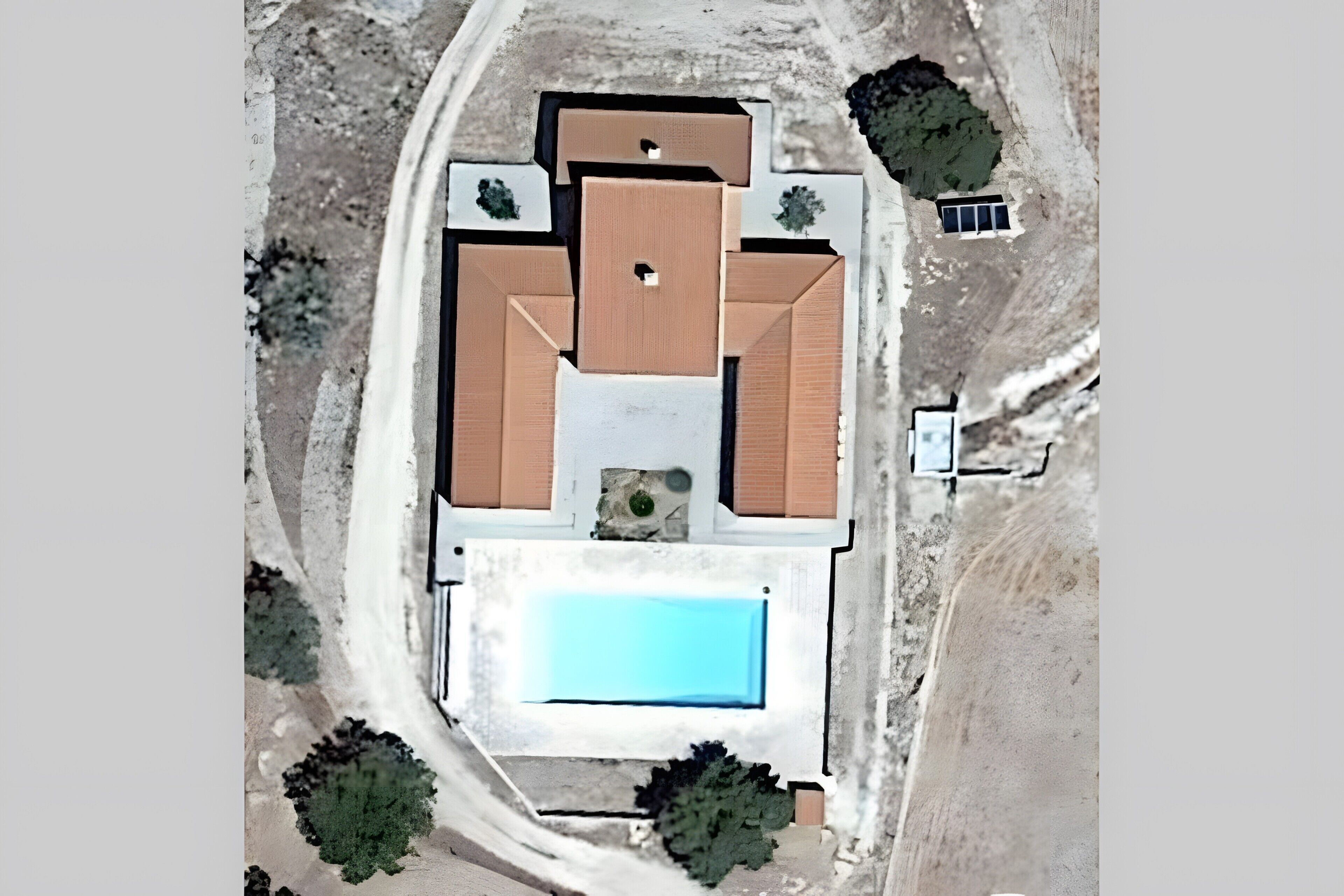 An aerial view of a house with a swimming pool, a large patio area, and several trees.