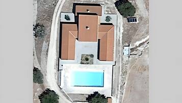 An aerial view of a house with a swimming pool, a large patio area, and several trees.