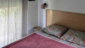Et soveværelse med sengegavl i træ, seng med blomstret sengetøj, hængende lysarmatur, et lille rundt bord og en vægmonteret lampe.