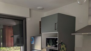 Et køkken med indbygget ovn, mikroovn og køleskab. Der er et vindue med udsigt til en have.