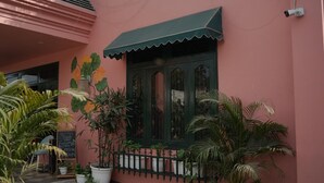 Een roze gebouw met een groen luifel, potplanten en een schoolbordreclamebord.