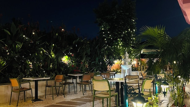 Een terras met tafels en stoelen, omringd door potplanten en sfeerverlichting.