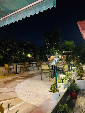 An outdoor seating area with tables and chairs, surrounded by potted plants and decorative lights. - Artistik Abode By Stay Banaras (Varanasi)
